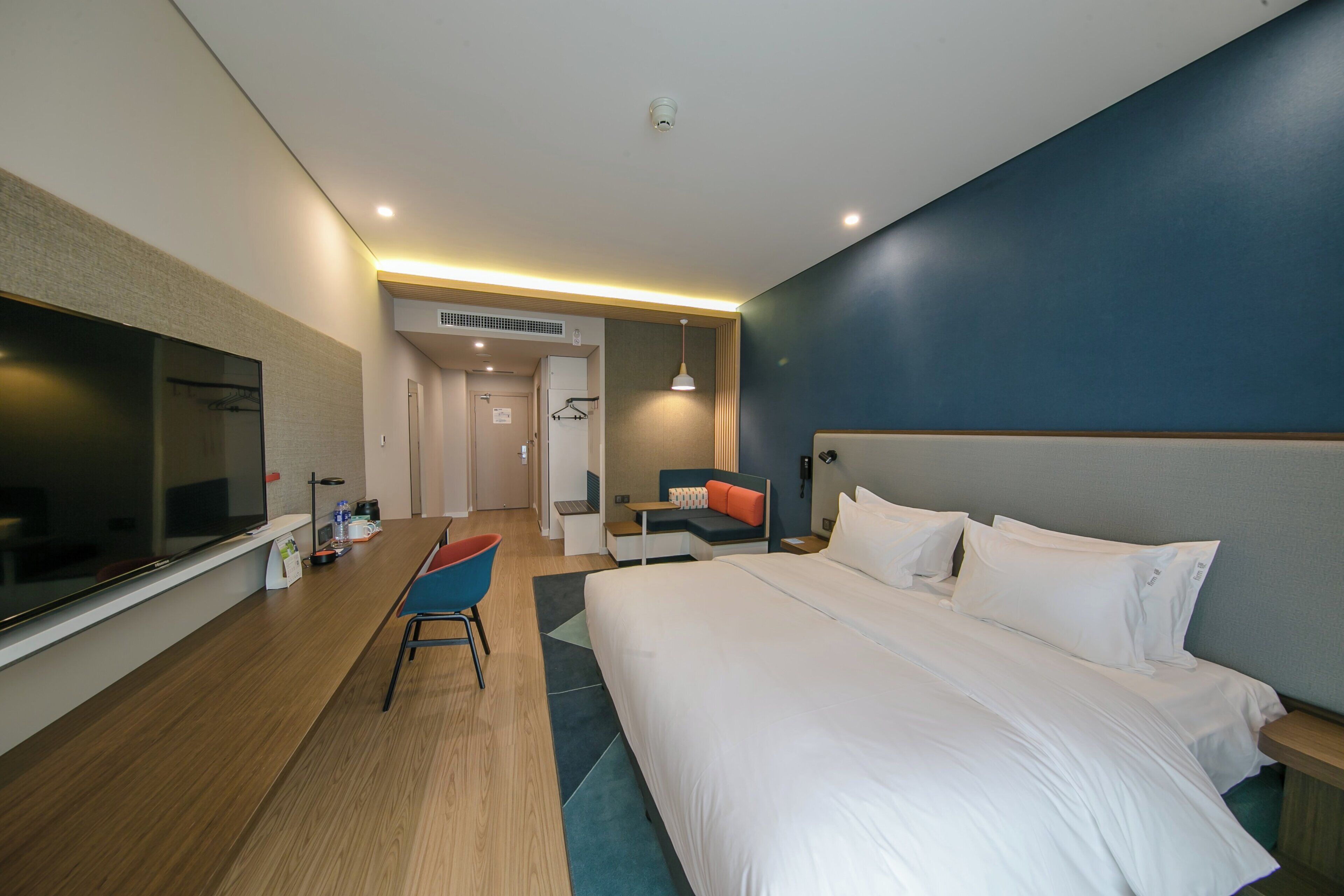 A hotel room with a large bed, a desk, a chair, a television, and a bathroom visible through an open door.