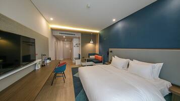 A hotel room with a large bed, a desk, a chair, a television, and a bathroom visible through an open door.