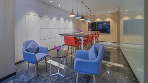 A modern interior with a dining area featuring a wooden table and red chairs, blue armchairs, and pendant lighting.