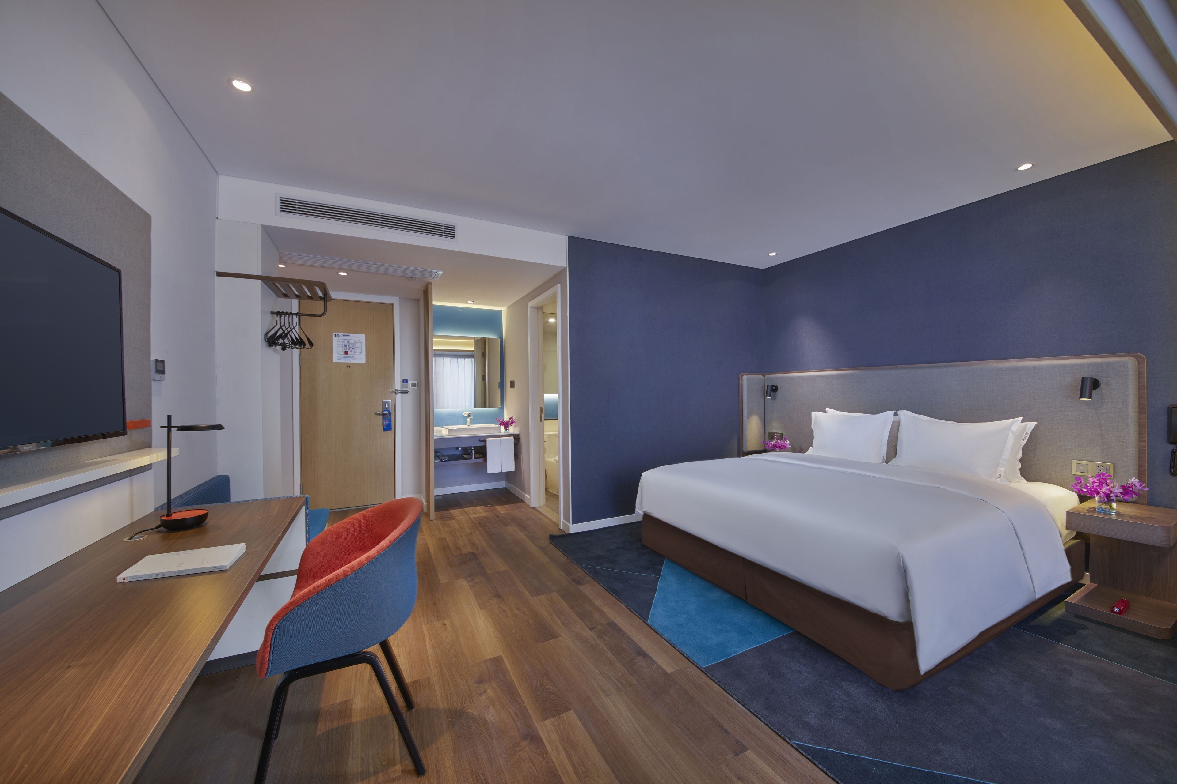 Een moderne hotelkamer met een groot bed, een bureau met stoel, een televisie en een badkamer zichtbaar door een geopende deur.