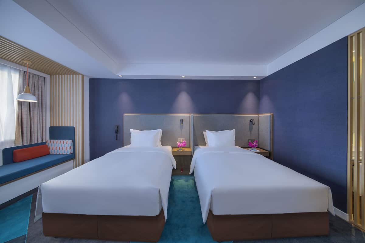 A hotel room with two beds, a seating area with a view, and a nightstand with a lamp.