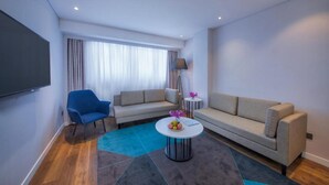 A modern living room with a sofa, a blue armchair, a coffee table with fruit, and a TV mounted on the wall. - Holiday Inn Express Shanghai Jinshan by IHG (Shanghai)