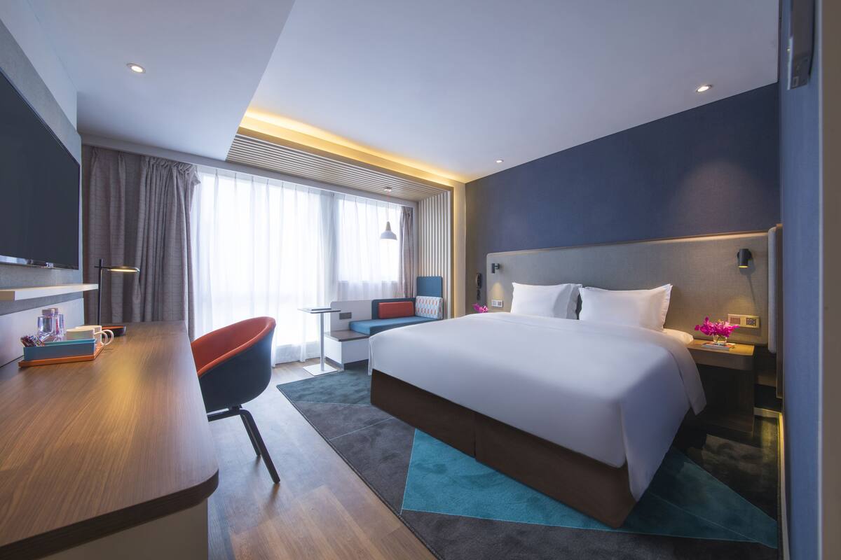 A modern hotel room with a large bed, a desk, a chair, and a TV.