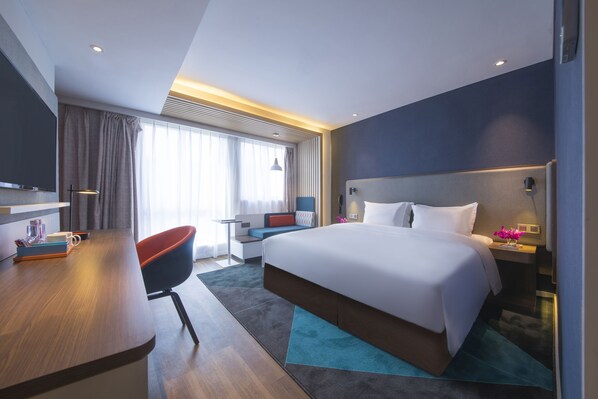 A modern hotel room with a large bed, a desk, a chair, and a TV.
