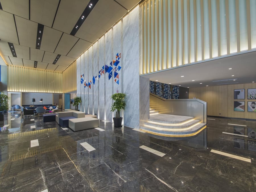 A modern lobby with a marble floor, seating area, and a staircase.