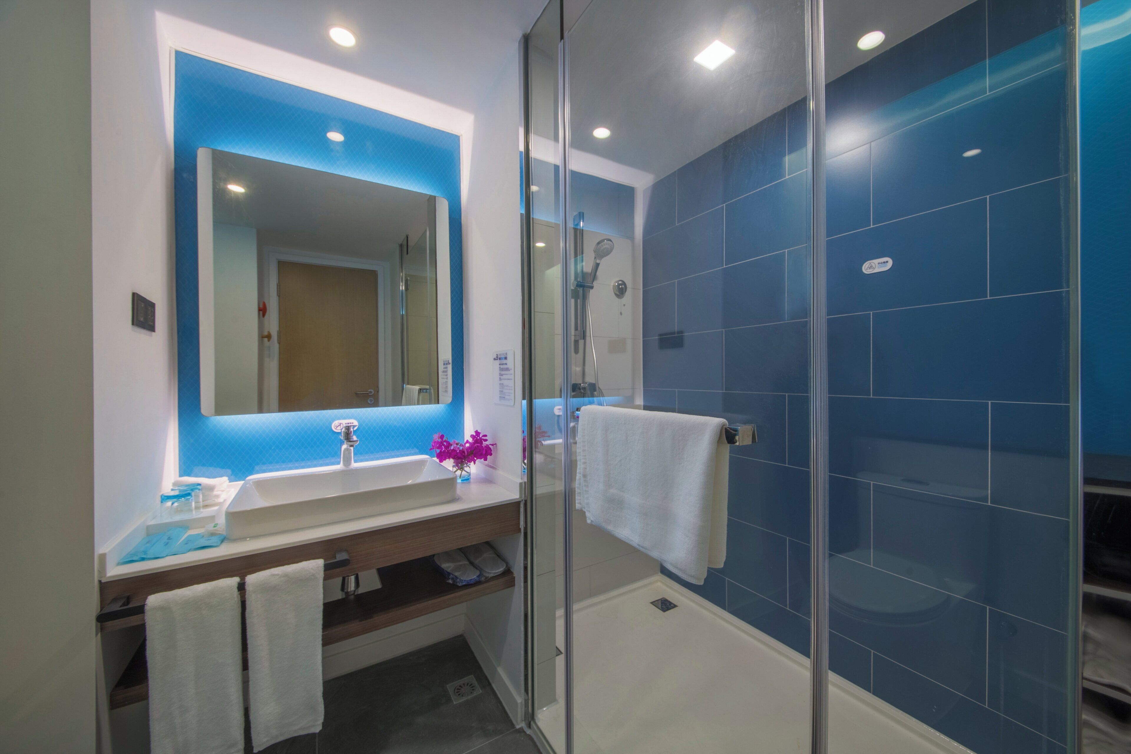 A modern bathroom with a glass shower enclosure, a white sink, and a blue-tiled shower wall.