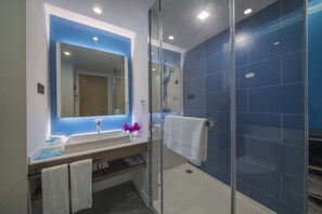 A modern bathroom with a glass-enclosed shower, a large mirror, and a white sink.