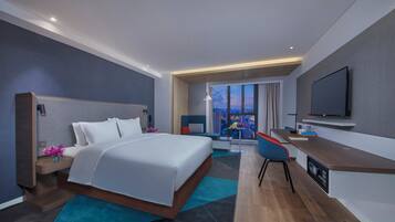 A modern hotel room with a large bed, a desk, a flat-screen TV, and a city view.