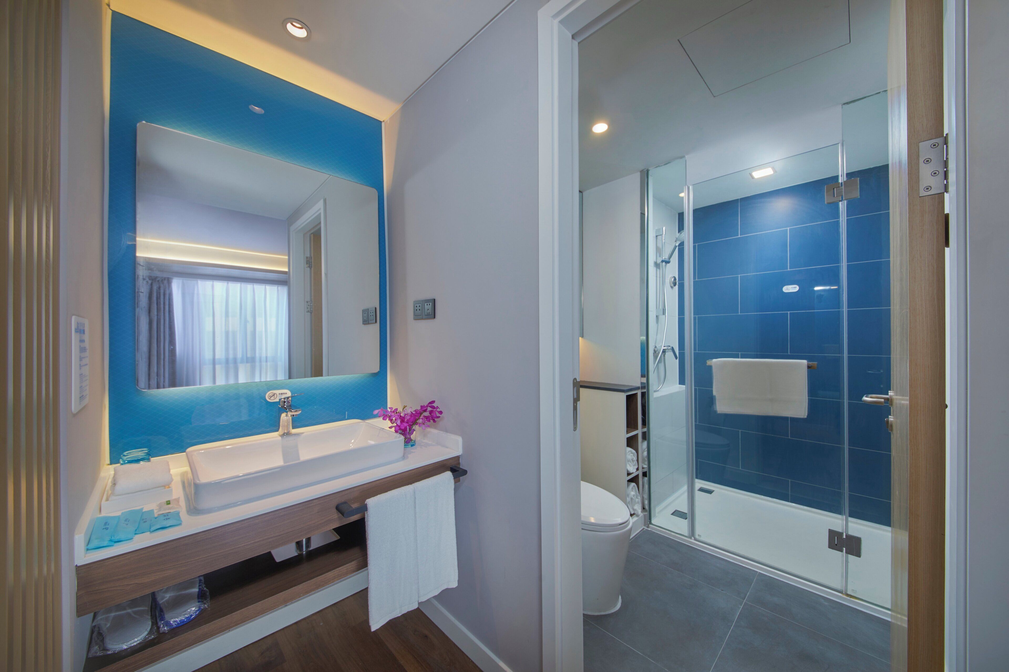 A modern bathroom with a large mirror, a sink, and a glass-enclosed shower.