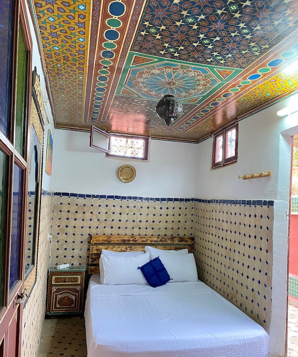 Una habitación con una cama, cabecera de madera, techo decorativo y una ventana pequeña.
