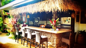 A bar area with a thatched roof, wicker chairs, and a stone counter.