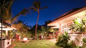 A well-maintained garden with a lawn, palm trees, and a barbecue area.