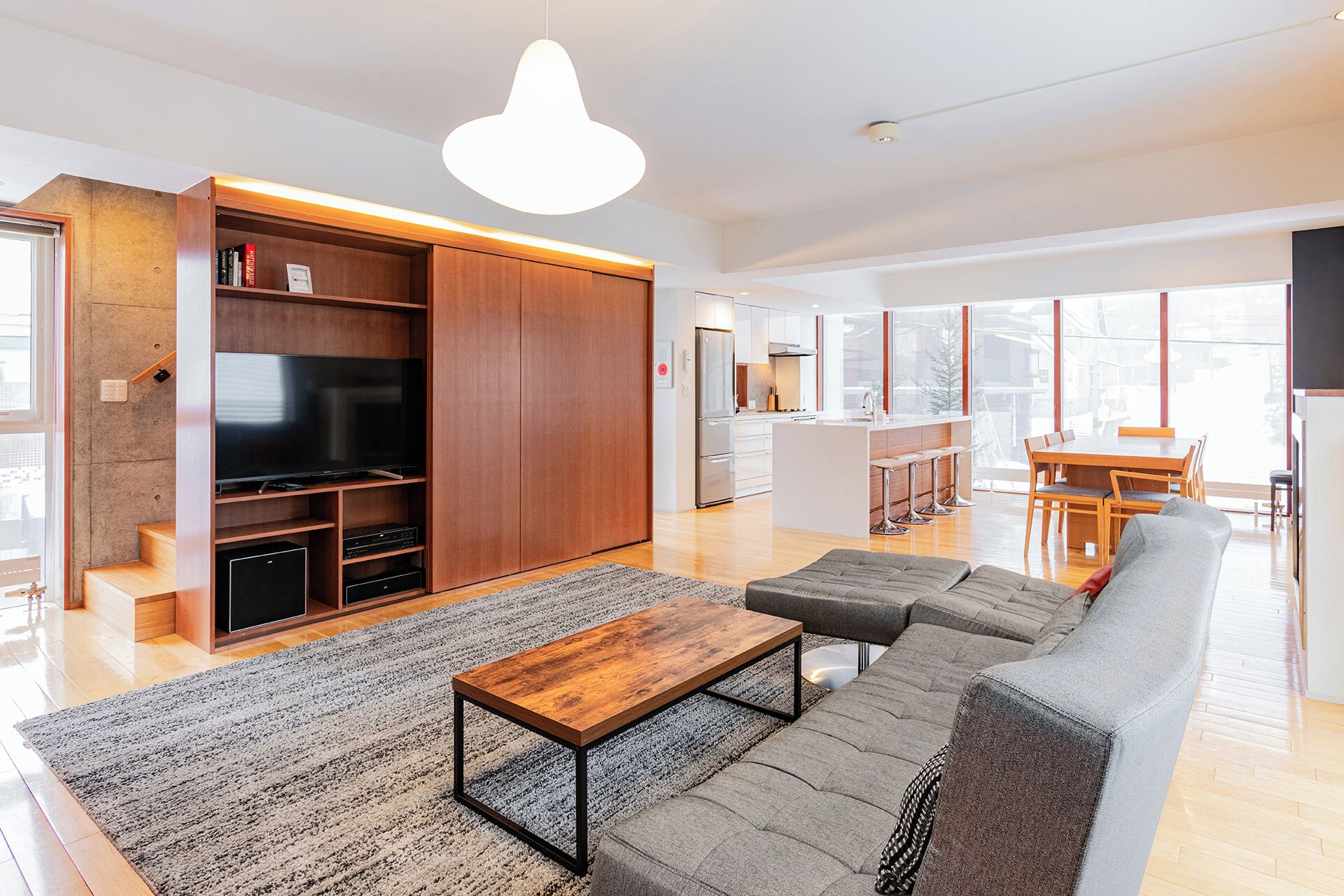 A modern living room with a sofa, coffee table, and TV. There is a kitchen area with a dining table and chairs.