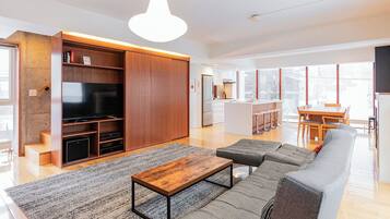 A modern living room with a sofa, coffee table, and TV. There is a kitchen area with a dining table and chairs.