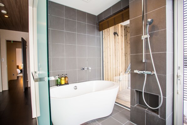 A modern bathroom with a freestanding bathtub, a glass shower enclosure, and a wooden door. - Niseko Central Houses and Apartments (Kutchan)