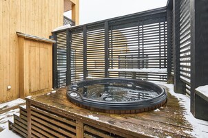 Un bain à remous sur une terrasse en bois, avec une clôture en bois et de la neige au sol.