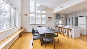 Una cocina moderna con una isla central, una zona de comedor con una mesa larga y ventanas amplias que permiten la entrada de luz natural.