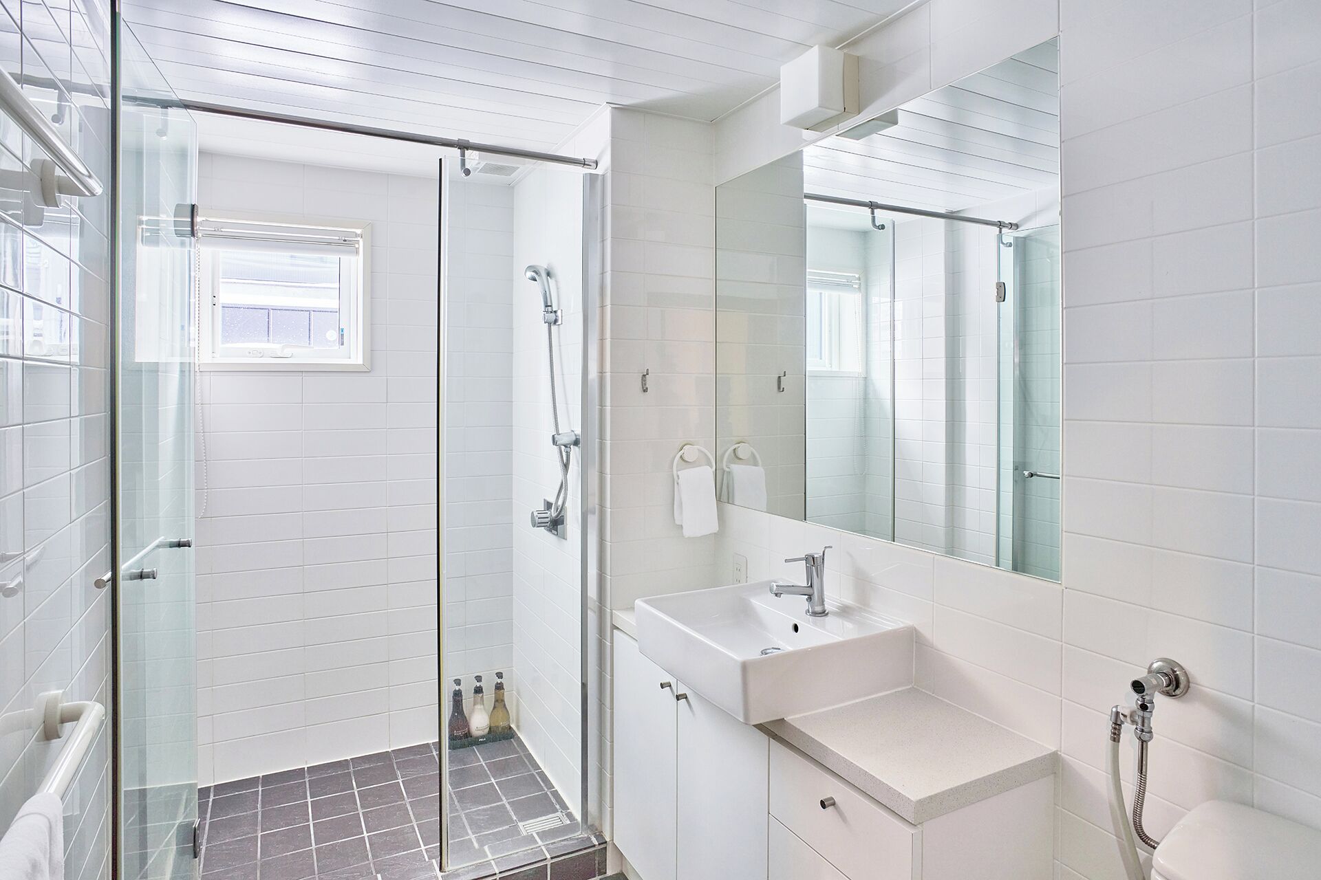 A modern bathroom with a glass shower enclosure, a white sink, and a large mirror.
