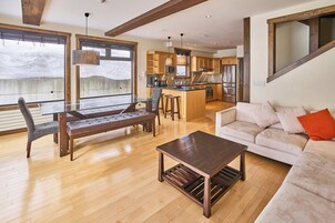 Un vaste espace de vie comprenant un banc en bois, un canapé et une table basse. On y trouve également une cuisine équipée d’appareils modernes et dotée d’une grande fenêtre.