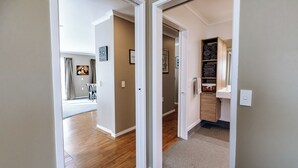 A hallway with wooden flooring, a door leading to a room with a bed and a window, and a small cabinet with towels. - Quiet Napier Retreat, close to the off-road trails (Taradale)
