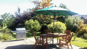 An outdoor patio with a grill, wooden table, chairs, and an umbrella. - Quiet Napier Retreat, close to the off-road trails (Taradale)