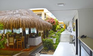 A hotel corridor with a thatched-roof outdoor seating area, a small garden, and a reception desk. - Hotel Ancor (Sincelejo)