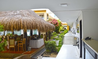 Un pasillo de hotel con una zona de estar al aire libre con techo de paja, un pequeño jardín y una recepción.