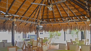 Restaurant amb teulada de palla, taules i cadires de fusta.