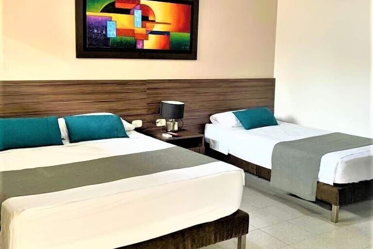 Une chambre d’hôtel avec deux lits, une table de chevet, une lampe et une peinture abstraite aux couleurs vives accrochée au mur.