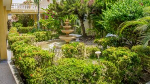 Jardí ben cuidat amb una font en terrasses, vegetació exuberant i un balcó amb plantes en test.