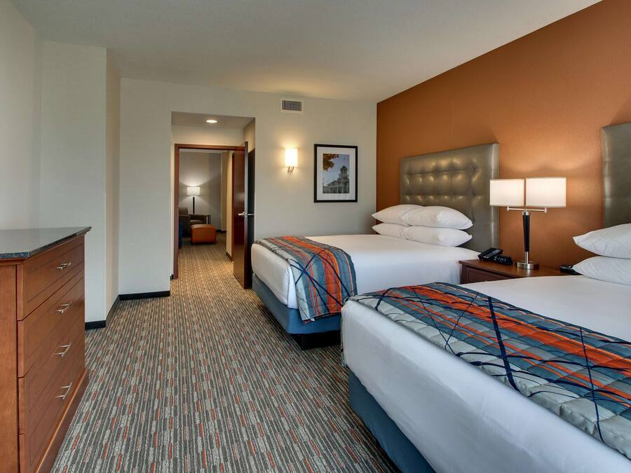A hotel room with two beds, a dresser, a nightstand with a lamp, and a framed picture on the wall.
