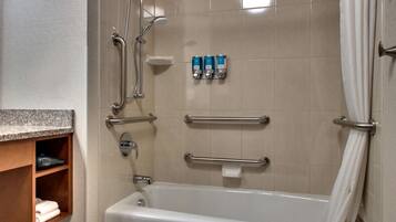 A bathroom with a bathtub, grab bars, and a shelf with towels.