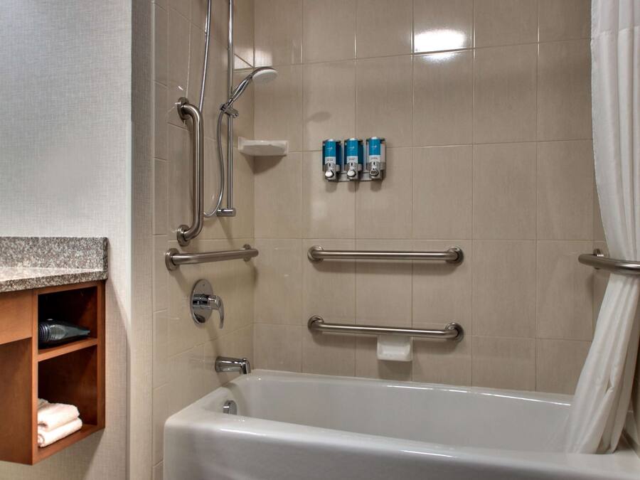 A bathroom with a bathtub, grab bars, and a shelf with towels.