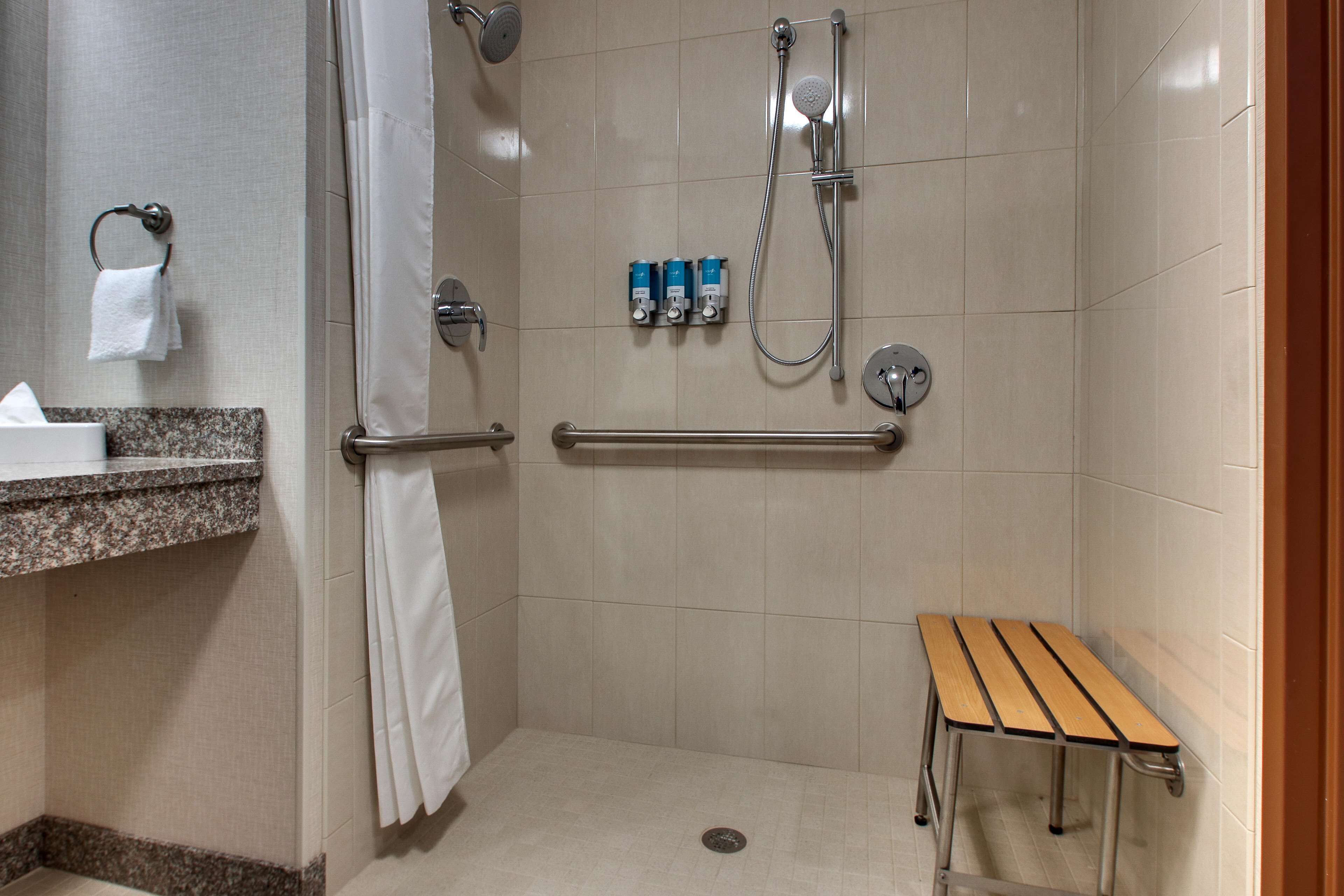 A shower area with a bench, grab bars, and a towel rack.