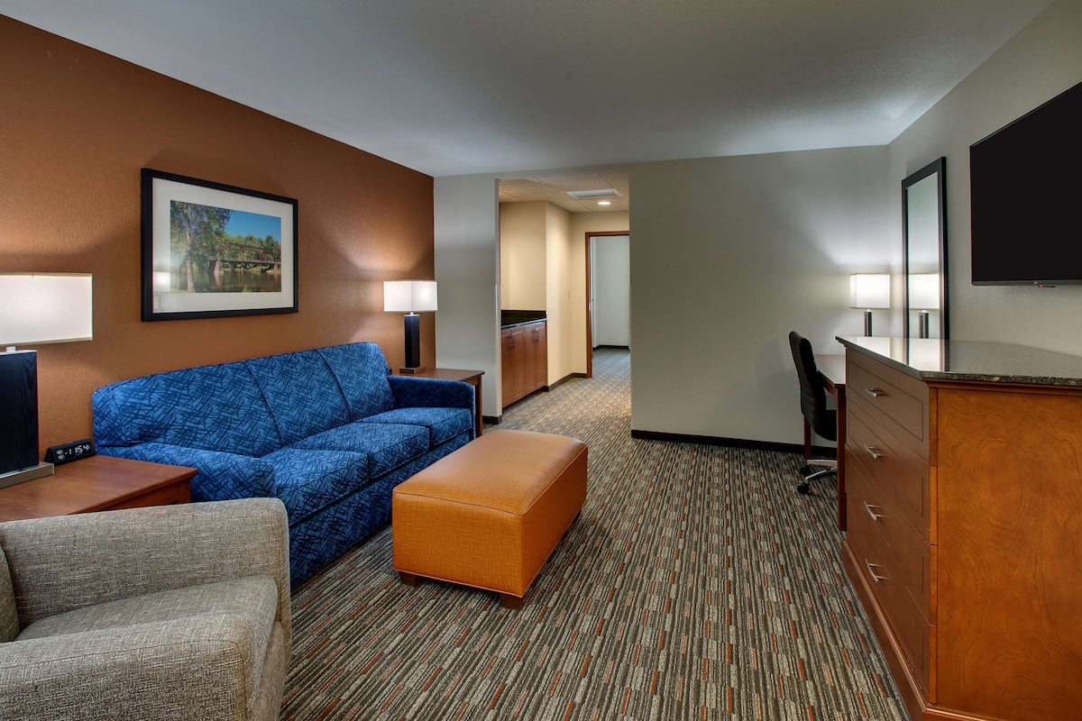 Une chambre d’hôtel avec un canapé bleu, un pouf orange, un bureau en bois et une télévision.