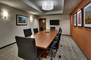 A conference room with a long wooden table, black chairs, a flat-screen TV, and framed pictures on the walls.