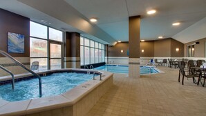 Un área de piscina interior con jacuzzi, zona de estar y ventanas amplias.