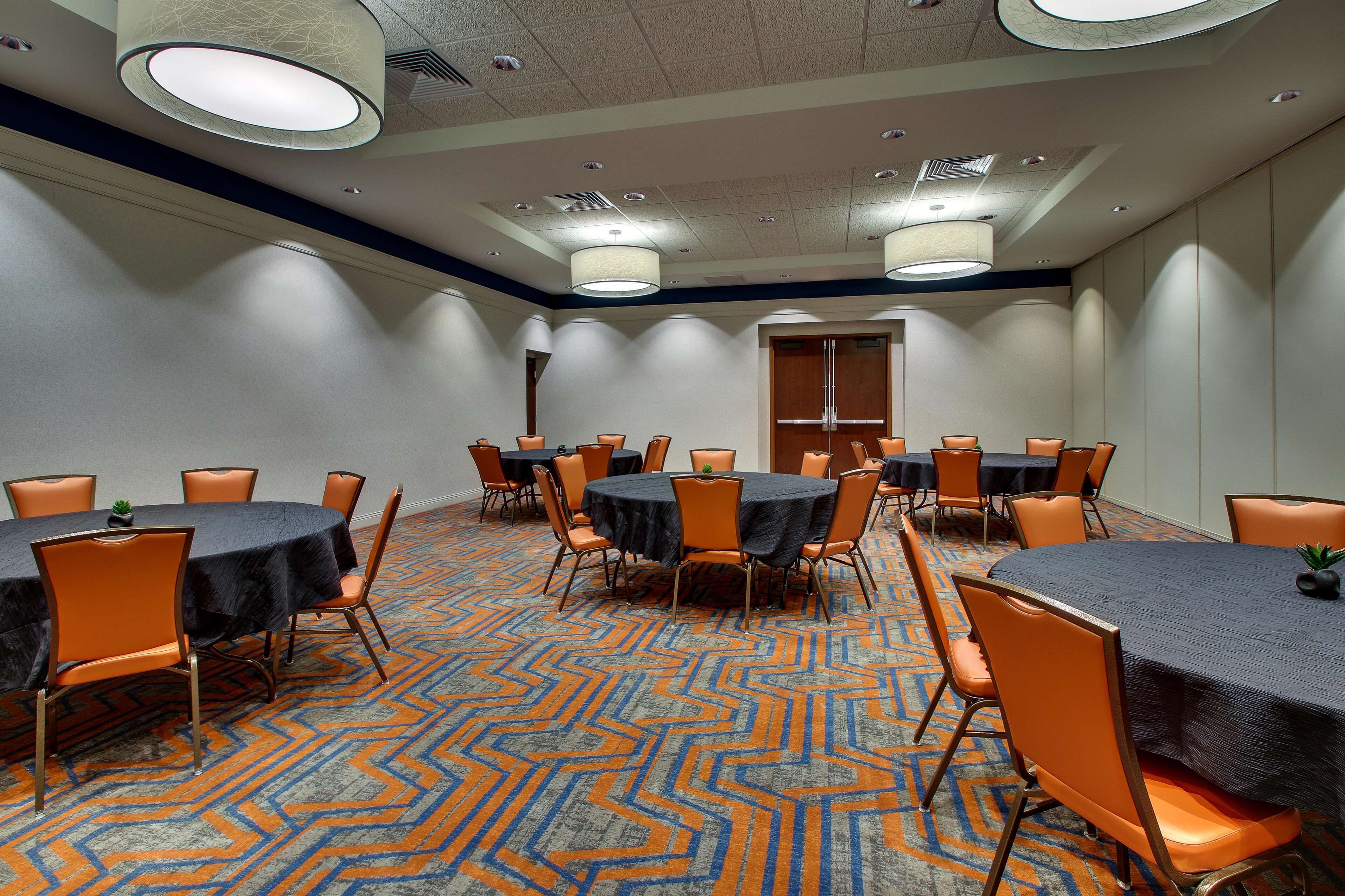 A conference room with multiple tables and chairs, carpeted floor, and ceiling lights.
