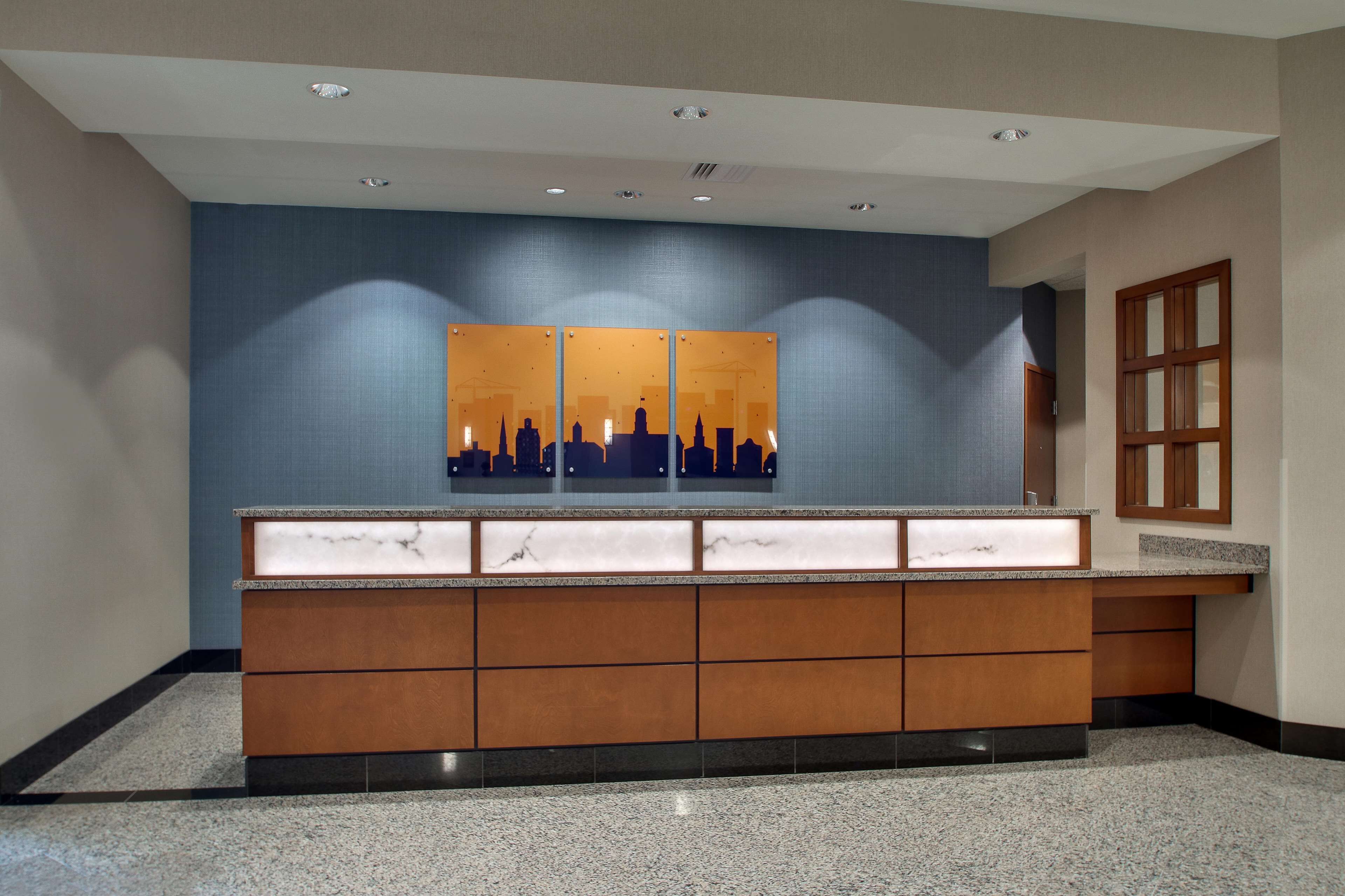 A reception area with a marble counter, wooden cabinets, and a cityscape artwork on the wall.