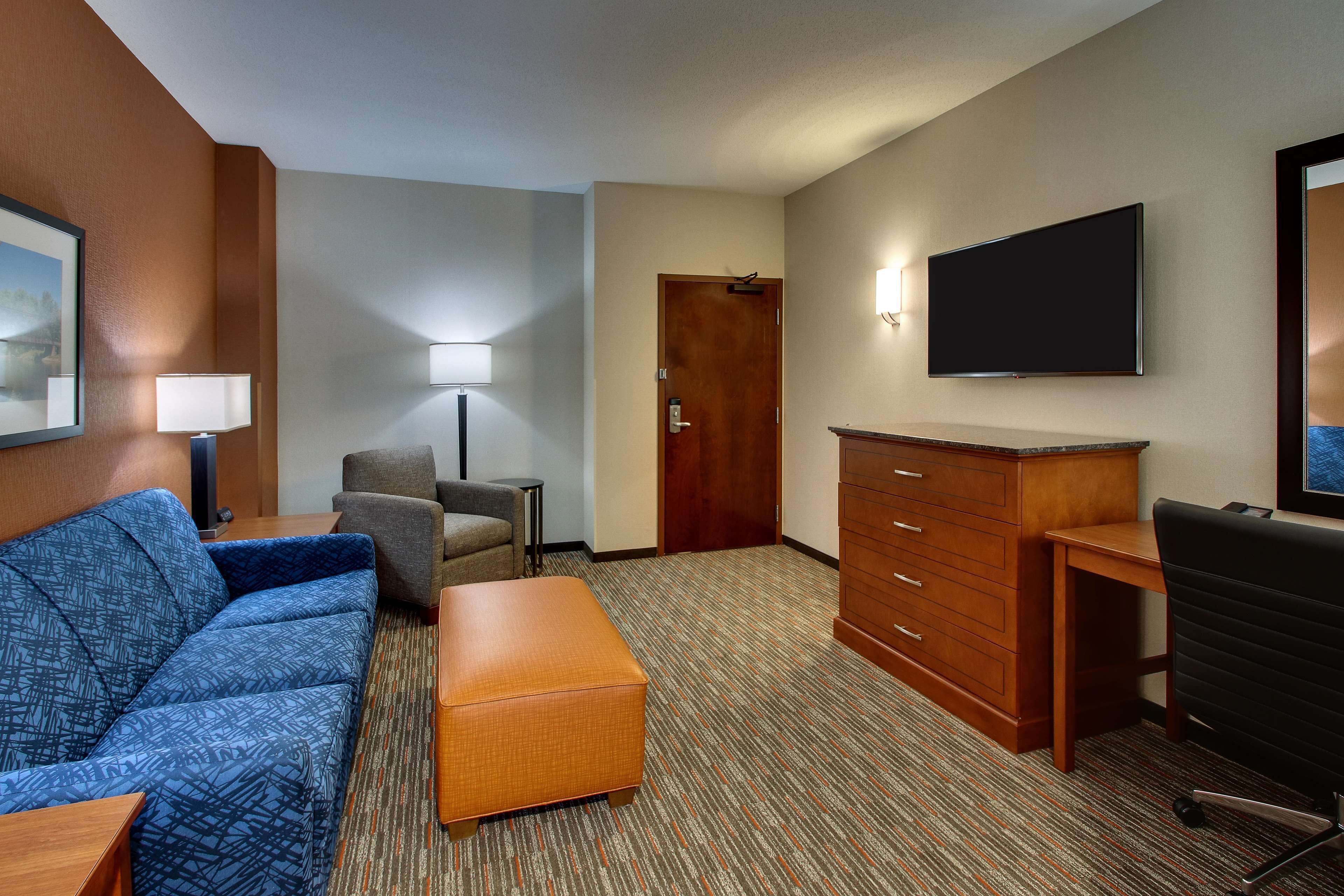 Habitación de hotel con un sofá azul, un escritorio de madera, un televisor y una puerta.