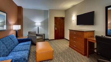 Habitación de hotel con un sofá azul, un escritorio de madera, un televisor y una puerta.