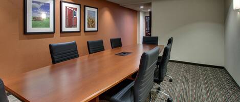 A conference room with a long wooden table, six black chairs, and three framed pictures on the wall.