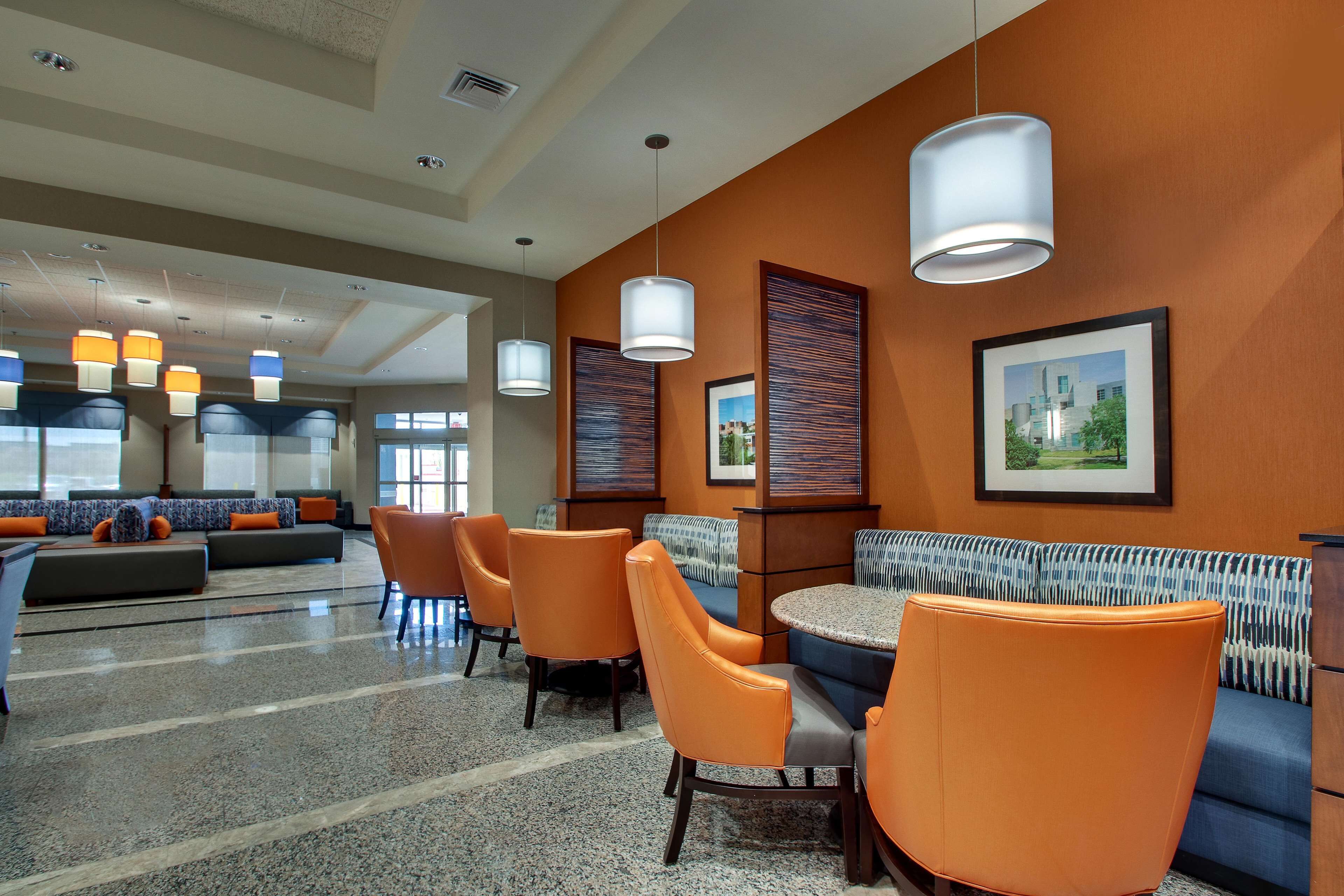 A modern hotel lobby with a seating area, a reception desk, and a large window providing a view of the outdoors.