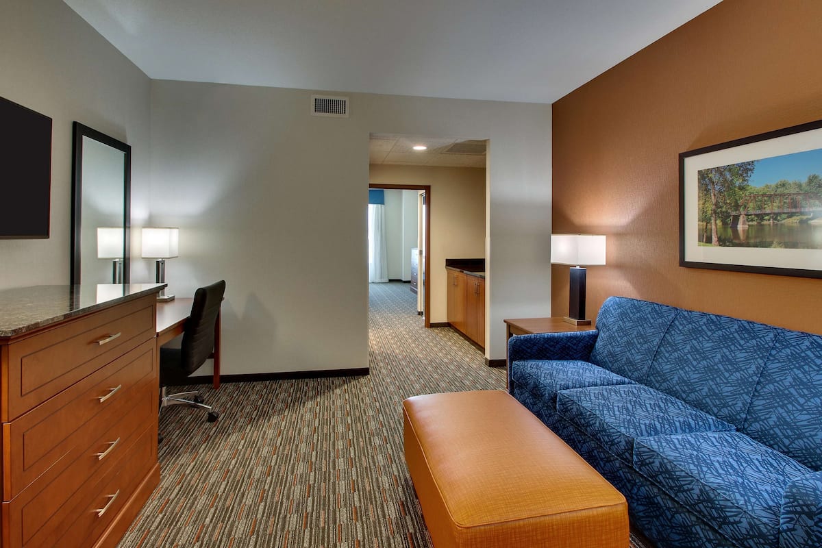 Une chambre d’hôtel équipée d’un bureau, d’une chaise, d’un canapé et d’un pouf. On y trouve également un miroir, une lampe et un tableau encadré au mur.