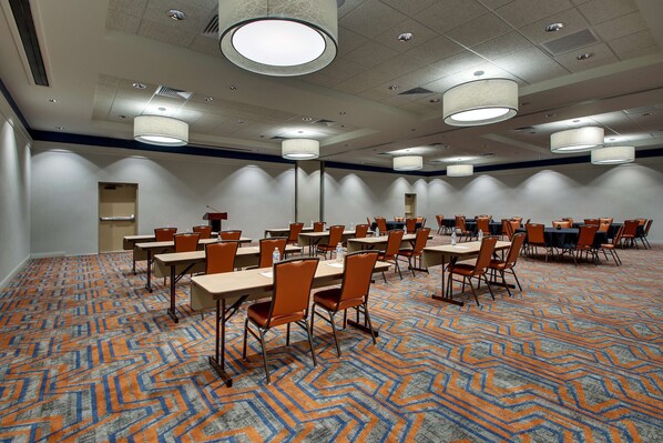 A conference room with multiple tables and chairs, arranged in rows, with a patterned carpet and ceiling lights.