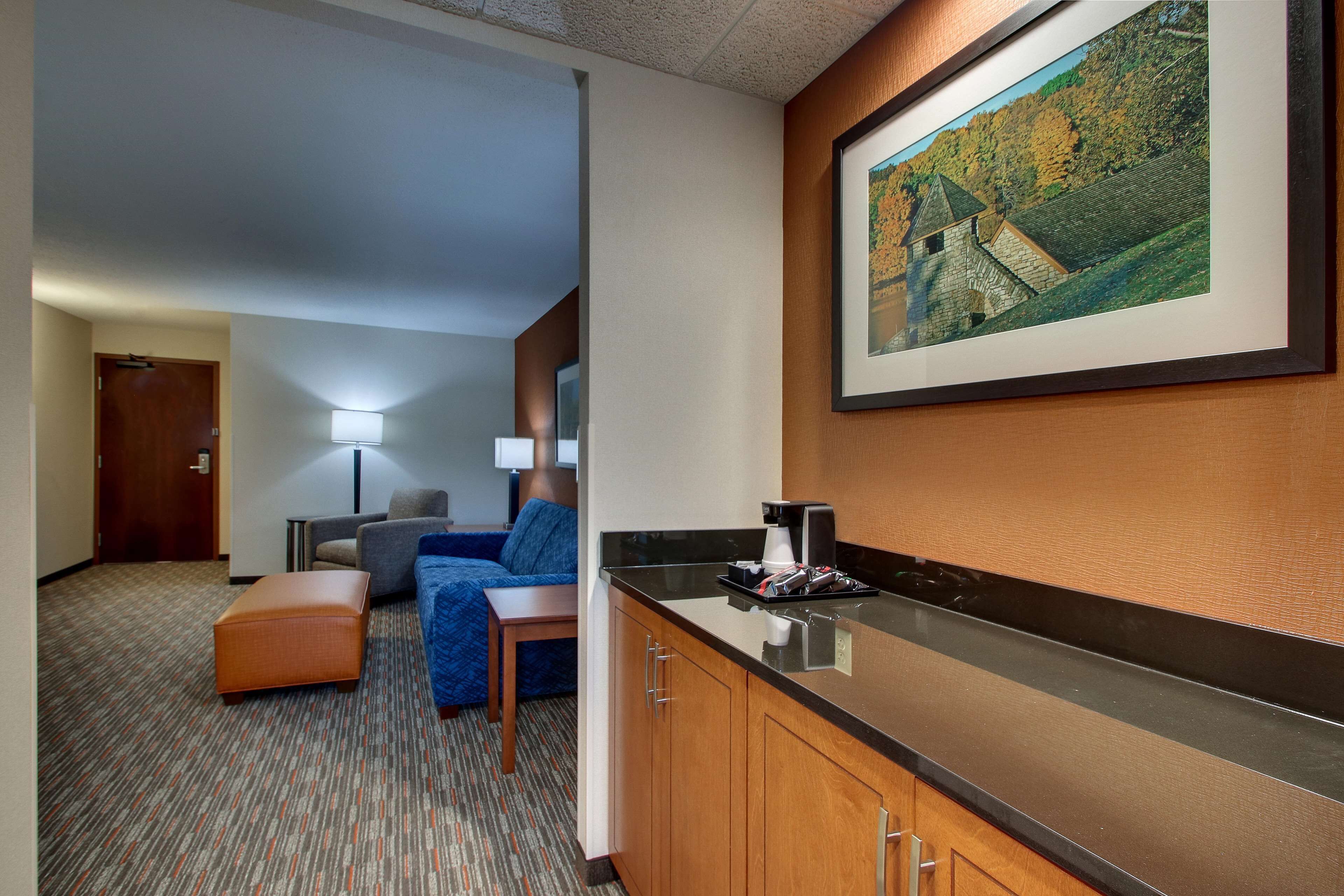 A hotel room with a kitchenette, a sofa, a desk, and a framed picture on the wall.
