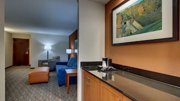 A hotel room with a kitchenette, a sofa, a desk, and a framed picture on the wall.
