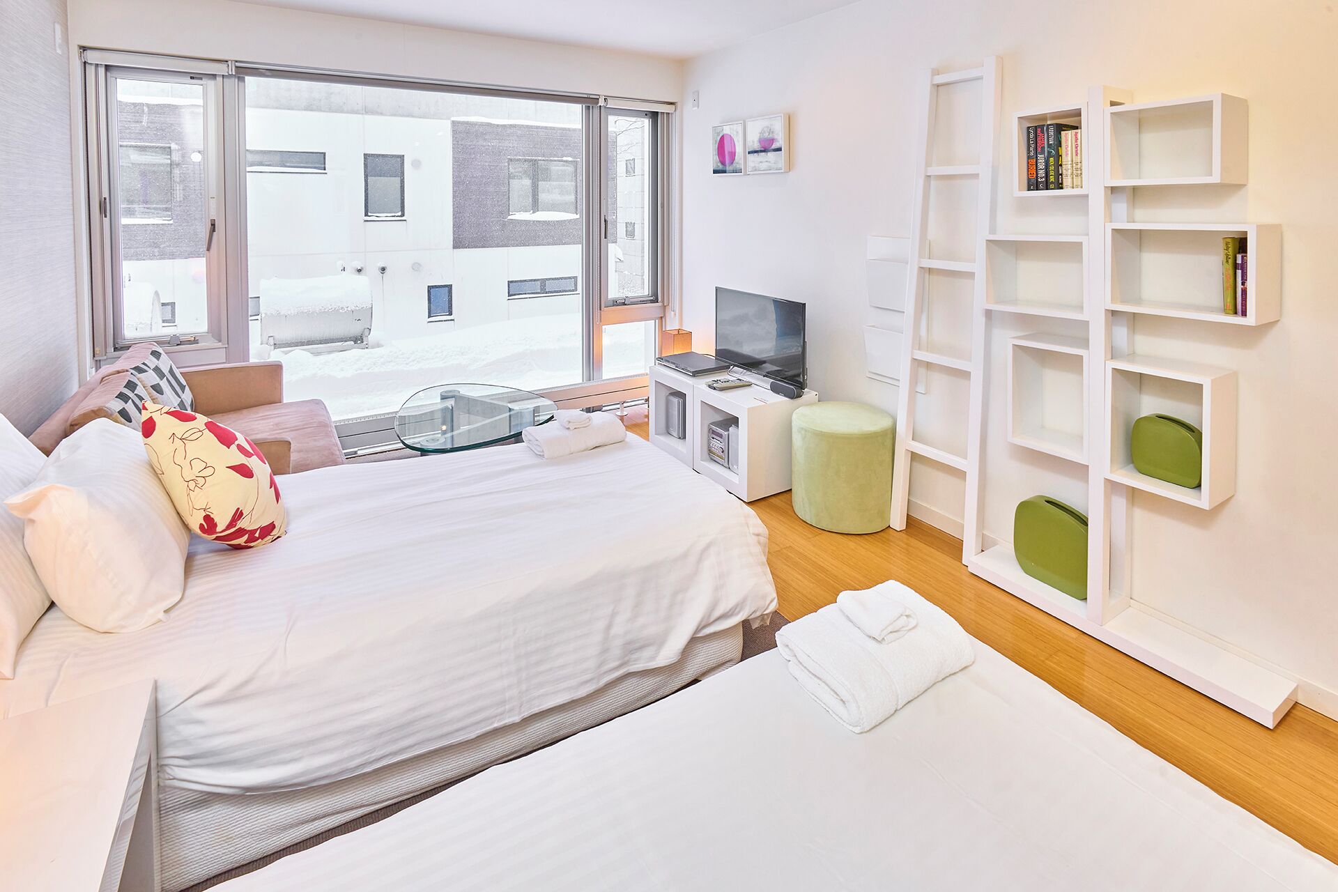 A hotel room with a bed, a TV, a small table, and a bookshelf.