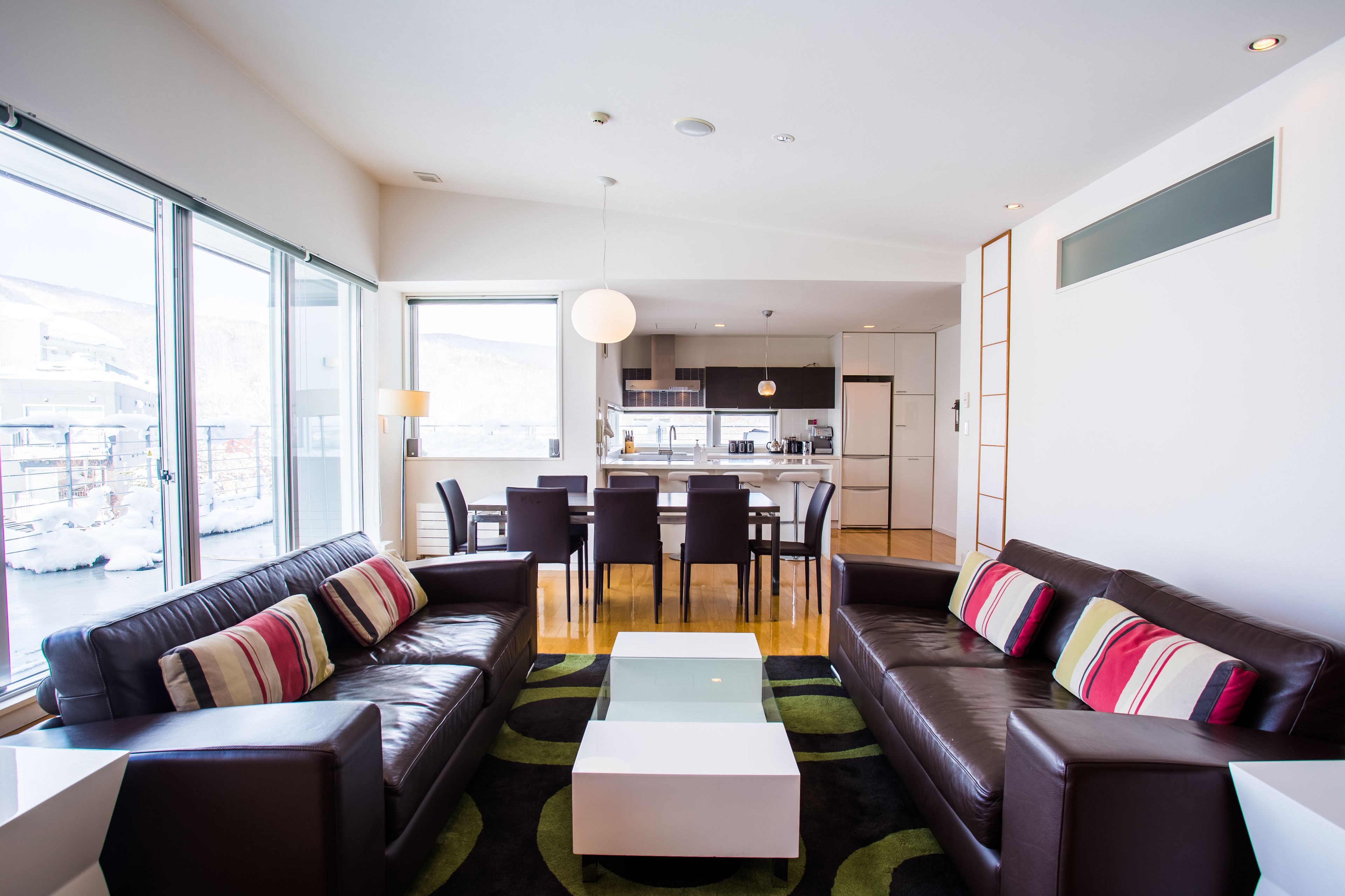 A modern living room with a sofa set, a coffee table, and a dining area with chairs and a kitchen in the background.