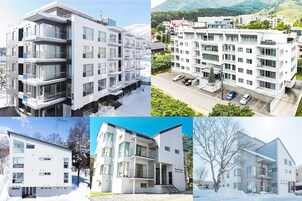Un immeuble moderne à plusieurs étages, doté de balcons, d’un espace de stationnement et offrant une vue sur un paysage vallonné.